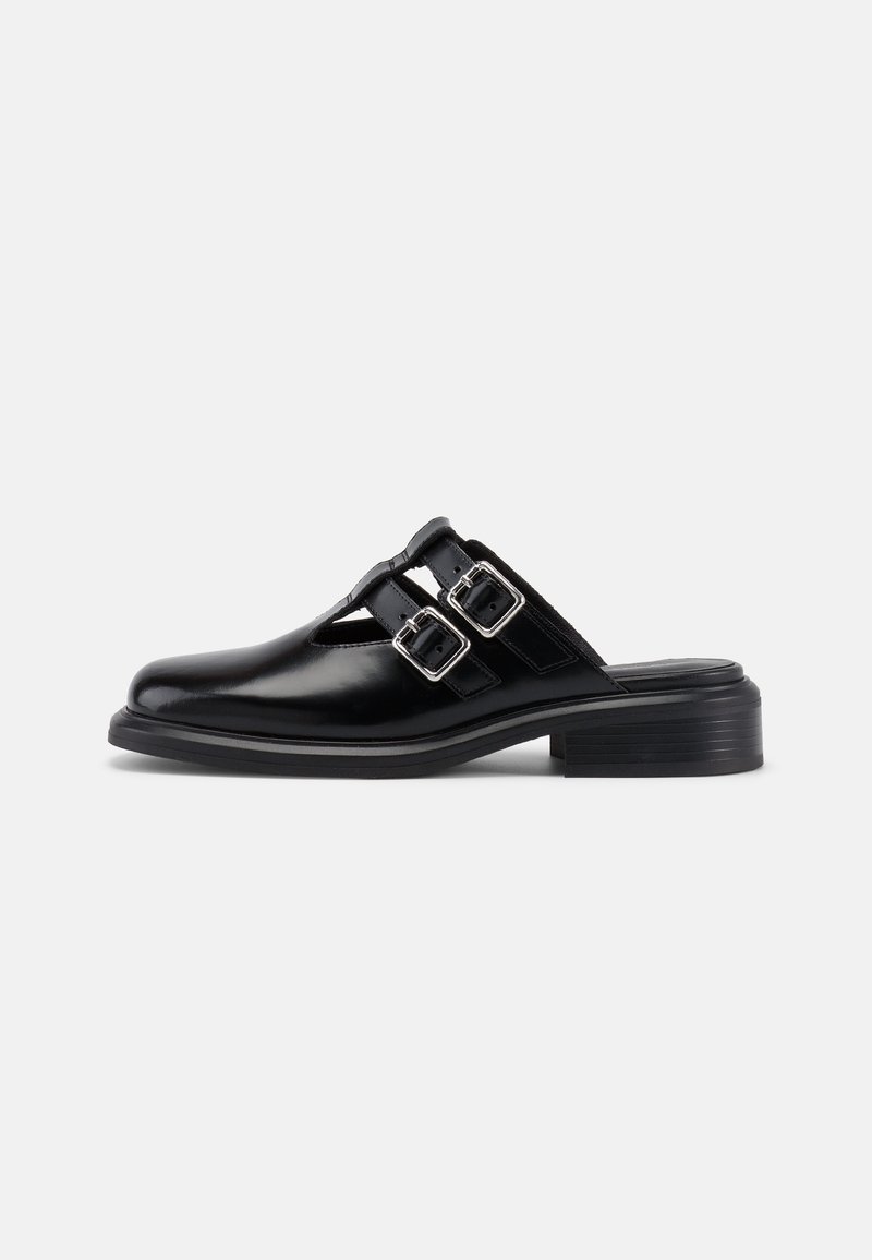 Chaussure en cuir noire à enfiler avec deux boucles argentées et détails découpés, petit talon empilé et bout arrondi.