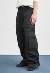Zwarte cargo broek met een wijde pijpdesign, voorzien van meerdere zakken, verstelbare boorden en een gladde, waterafstotende stof.