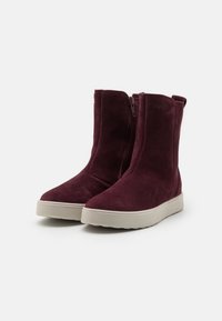 Paire de bottes mi-mollet en daim bordeaux avec fermetures éclair latérales et semelles épaisses en caoutchouc blanc sur fond blanc.