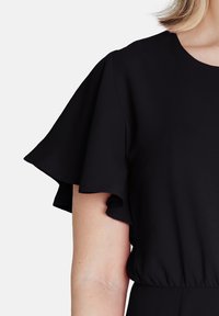 Černé šaty s krátkými volánkovými rukávy, kulatým výstřihem, elastickým pasem a hladkou matnou texturou látky.