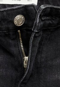 Black denim fabric featuring a metal zipper and snap button closure. Close-up reveals stitching details and a smooth texture.
