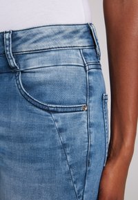 Jeans de denim azul deslavado con un corte ajustado, que cuentan con un bolsillo para monedas, costuras a tono y un pequeño detalle de botón de metal en la parte frontal.