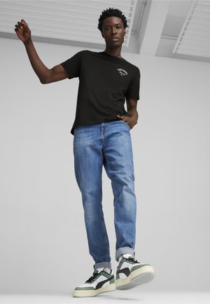 Sort bomuld t-shirt med grafisk print, blå lige bukser og hvid-grønne sneakers med sorte accenter. Let teksturerede stoffer.