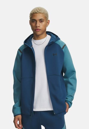 Blauwe capuchontrui met rits en contrasterende teal mouwen, gemaakt van zacht materiaal, voorzien van een capuchon, voorzakken en een klein logo op de borst.