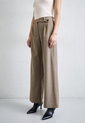 Woman wearing high-waisted wide-leg khaki trousers with side button detail and black pointed-toe heeled ankle boots.