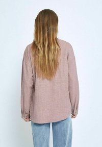 Light pink long-sleeve shirt made of textured fabric, featuring a loose fit and buttoned cuffs, paired with light blue relaxed-fit jeans.