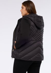 Černá prošívaná puffer vesta s kapucí, s diagonálním prošíváním, zapínáním na zip v předních kapsách a přiléhavým střihem.