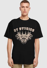 Černé bavlněné tričko s grafickým designem třech psích hlav a hrotů, s textem "2Y STUDIOS" v béžové barvě nad uměním.