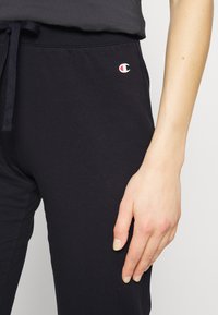 Svarta joggerbyxor i mjuk bomullsblandning, med elastisk midja och dragsko samt en liten vit och röd logotyp på vänster ben.