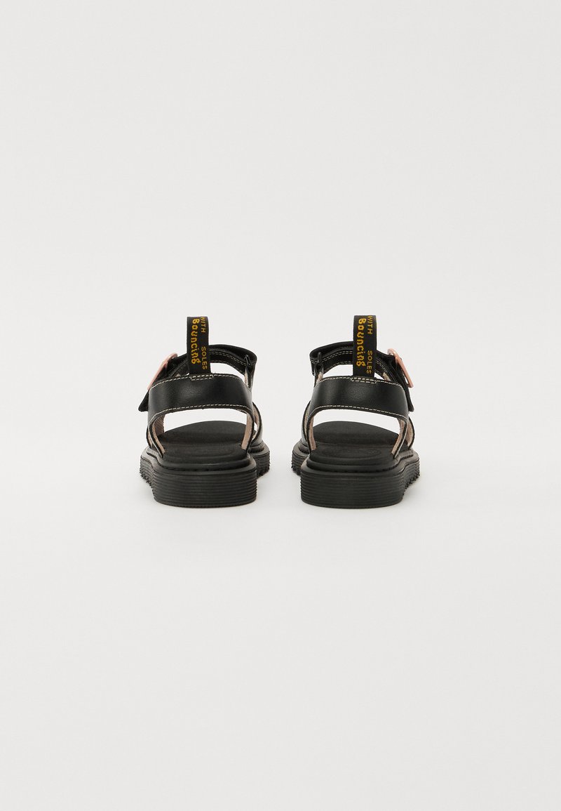 Sandales en cuir noir avec un dos ouvert, des sangles réglables et des semelles texturées. Présente un logo jaune sur le talon et des accents roses sur le côté.