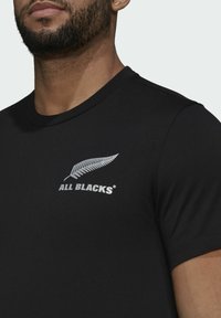 Mustat lyhythihaiset t-paidat, jotka on valmistettu puuvillasta ja joissa on pyöreä kaula-aukko. Rinnassa on valkoinen saniaismotiivi ja "ALL BLACKS" -teksti.