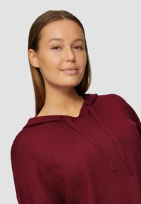 Bordeaux hoodie met een v-hals, trektouwtjes en een zachte textuur. Heeft een ontspannen pasvorm en minimale details, ontworpen voor comfort en veelzijdigheid.