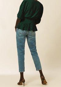 Blusa verde con texture, maniche a palloncino, vita peplum, abbinata a jeans a gamba dritta blu chiaro e sandali neri con tacco alto.