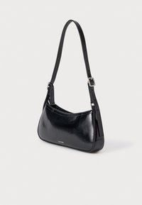 Μαύρη τσάντα από συνθετικό δέρμα με καμπύλη σχεδίαση, ρυθμιζόμενο λουρί και ασημένια μεταλλικά μέρη. Διαθέτει λεπτό λογότυπο μπροστά.