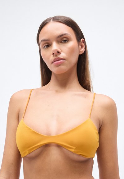 Haut de bikini jaune avec des bretelles fines, des bonnets triangulaires et une texture lisse. Le design minimaliste met en avant la simplicité et le style moderne.