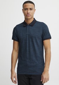 Navyblaues Polohemd aus strukturiertem Stoff, schwarzer Kragen, kurzärmlig und mit einer Knopfleiste mit zwei Knöpfen. Schlank geschnitten, minimalistische Akzente.