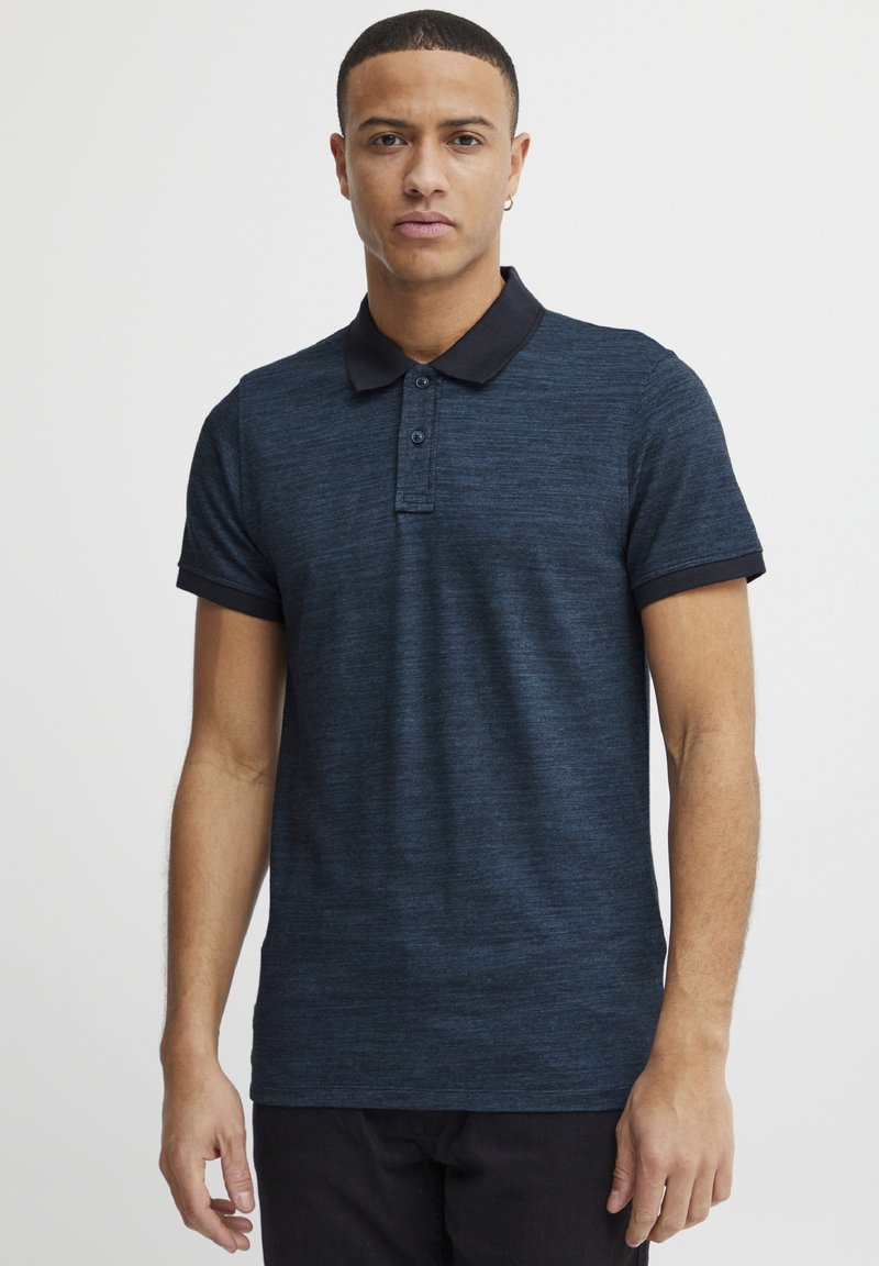 Navyblaues Polohemd aus strukturiertem Stoff, schwarzer Kragen, kurzärmlig und mit einer Knopfleiste mit zwei Knöpfen. Schlank geschnitten, minimalistische Akzente.