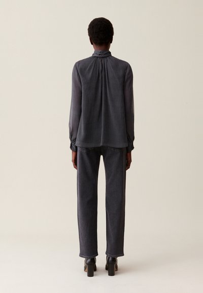 Blusa negra fluida con un cuello alto, diseño texturizado de rayas finas. Combinada con jeans oscuros de pierna recta y tacones gruesos negros.