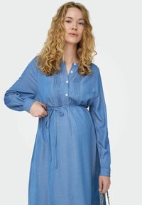 Jasnoniebieska sukienka ciążowa z długimi rękawami, guzikami z przodu, plisowanymi detalami i wiązaniem w talii. Wykonana z miękkiego, teksturowanego materiału.