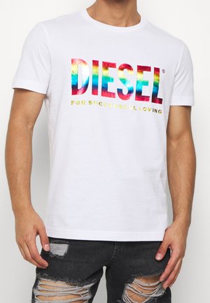 Witte T-shirt met korte mouwen met een multicolore reflecterende 'DIESEL'-logo en gouden tekst eronder, gedragen met versleten zwarte spijkerbroek.