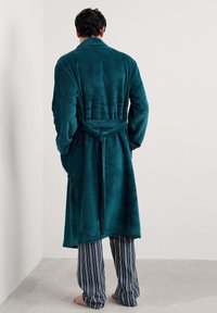 Tirkizni ogrtač s mekom, teksturiranom površinom, s remenom na struku, uparen s tamnoplavim i bijelim prugastim hlačama, nošen bosi.