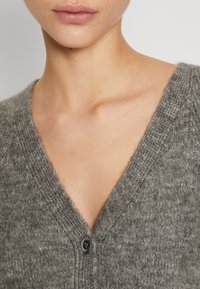 Szary sweter ze splotu z dekoltem w serek, z zapięciem na guziki i miękką fakturą. Ozdobiony subtelnym wzorem. Lekki i luźny krój.