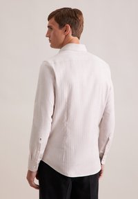 Camicia a maniche lunghe color beige chiaro in tessuto texture, con polsini abbottonati e un leggero svolazzo. Presenta un colletto classico e sottili righe verticali.