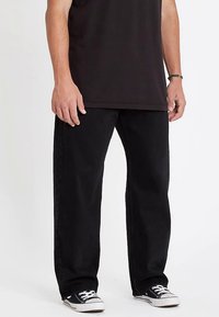 Black denim jeans with a relaxed fit, straight leg, subtle stitching details, and worn with black and white sneakers on a light background.