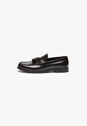 Brown leather loafers with a smooth finish, featuring a stitched design and decorative tassels on the front. Flat sole and round toe.
