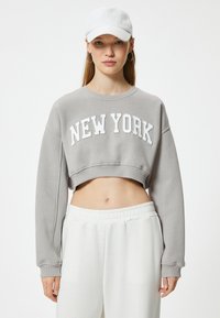 Felpa grigia corta con la scritta "NEW YORK" in lettere bianche, maniche lunghe e finitura testurizzata; abbinata a pantaloni bianchi con vita elastica.