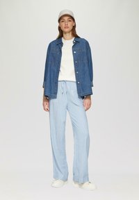 Denim jack, witte trui, lichtblauwe gestreepte broek en witte sneakers. De jack heeft twee zakken en een relaxte pasvorm, met opgerolde mouwen.