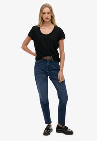 Czarna koszulka z krótkim rękawem o okrągłym dekolcie, zestawiona z niebieskimi jeansami o wysokim stanie. Czarne lakierowane mokasyny i pleciony pasek dopełniają stylizację.