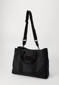 Czarna torba na ramię wykonana z wytrzymałego materiału, z dwoma uchwytami u góry, regulowanym paskiem na ramię oraz teksturowaną prostokątną łatką.