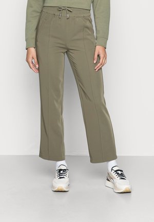 Calças desportivas verde oliva com cintura ajustável, apresentando bolsos laterais e um design de perna reta, combinadas com ténis brancos e beges.