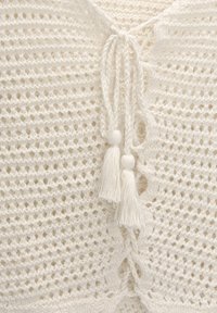 Maglione bianco lavorato a maglia con un design a trama aperta, legato con corde intrecciate e rifinito con pon pon decorativi.