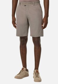 Bermuda beige da uomo realizzati in tessuto morbido, con vestibilità su misura, parte frontale liscia e tasche laterali discrete. Abbinati a sneakers beige chiare.