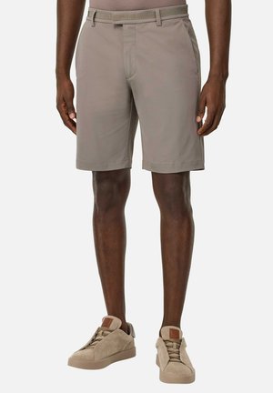 Shorts beiges pour hommes en tissu doux, avec une coupe ajustée, un devant plat et des poches latérales discrètes. Associés à des baskets beiges claires.