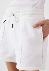 Pantaloni corti bianchi in misto cotone con elastico in vita e cordoncino. Presentano tasche laterali e cuciture a vista lungo le cuciture.