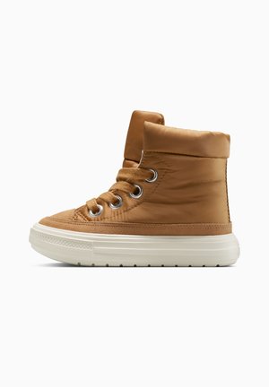 Zapatillas altas marrones con parte superior acolchada, puntera redonda, suela de goma blanca, ojales de metal y cordones marrones. Materiales suaves y texturizados.