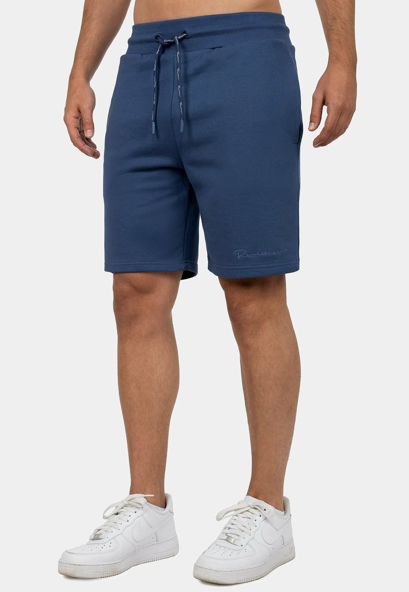 Marineblauwe sportbroek met een elastische tailleband, trekkoord en twee zijzakken; zachte textuur met subtiele logo-details aan de zoom.