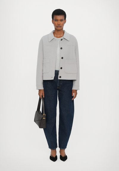 Light gray jacket with a straight cut, front pockets, and button closure, paired with dark blue jeans and black pointed flats.