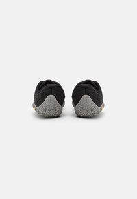 Schwarze Sportschuhe mit einer strukturierten Gummisohle, die ein graues Sohlenmuster und Branding an der Ferse aufweisen. Obermaterial aus glattem Stoff.