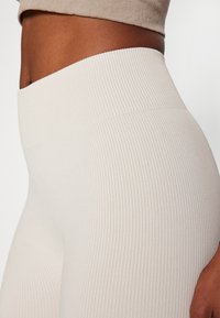 Leggings od off-white boje s rebrastim uzorkom i visokim pojasom, s glatkom teksturom i bešavnom dizajnom, naglašavajući prilagođenu siluetu.