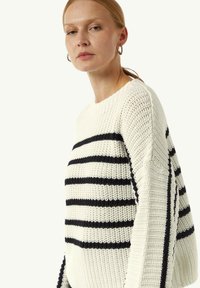 Sweter dzianinowy w oversize'owym kroju, z kremowym tłem i granatowymi poziomymi paskami. Ribbowany dekolt i teksturowana tkanina.