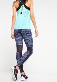 Un débardeur de sport bleu clair avec un dos nageur, assorti à des leggings noirs et violets à motifs, dotés d'accents en maille, et des baskets noires.