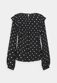 Blusa nera con pois bianchi, maniche a ruches, apertura a chiave sul retro e vita arricciata. Tessuto morbido dal tocco liscio.