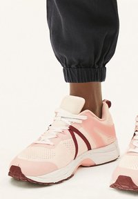 Baskets de sport rose clair en matériau en mesh et synthétique, avec des lacets blancs et des accents bordeaux. Semelle en caoutchouc avec grip texturé.