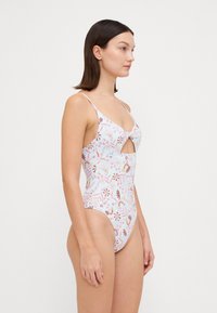 Maillot de bain une pièce dans des couleurs pastel légères avec des motifs floraux. Présente une découpe en forme de trou de clé et des bretelles fines. Matière lisse, couverture moyenne.