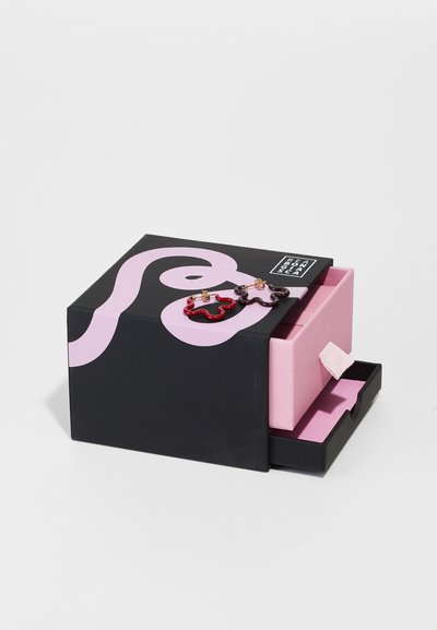 Schwarze Schmuckschatulle mit einem pinken abstrakten Design, ausgestattet mit einer kleinen pinken Schublade. Rote und dunkelrosa blumenförmige Ohrringe liegen obenauf.