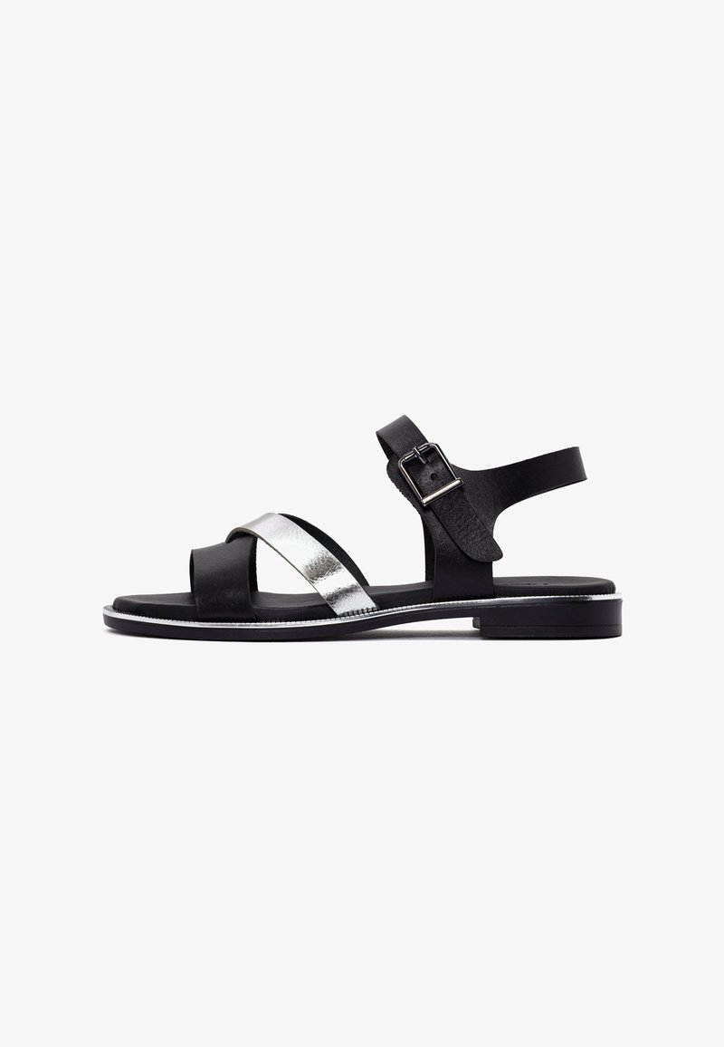 Black and silver leather sandals with an open toe, two crisscross straps, adjustable ankle strap, and a low, flat sole.